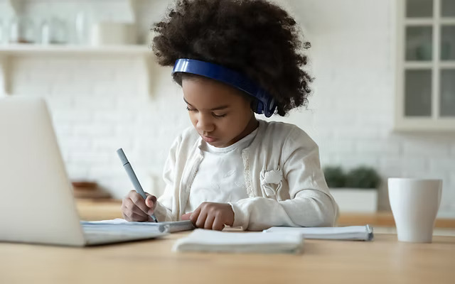 Young child wearing headphones and writing maths work at home