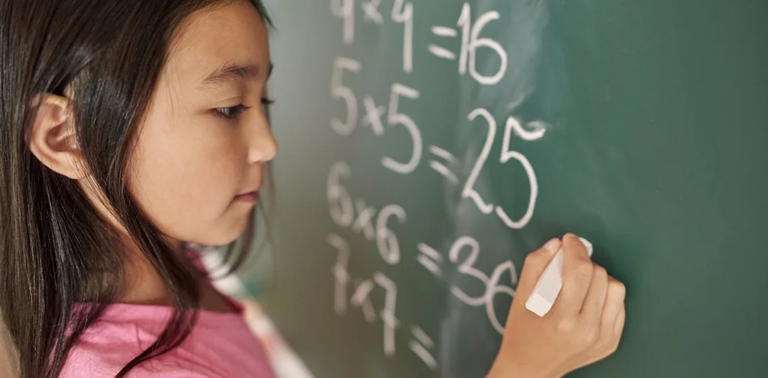 Young child writing maths answers on a classroom board